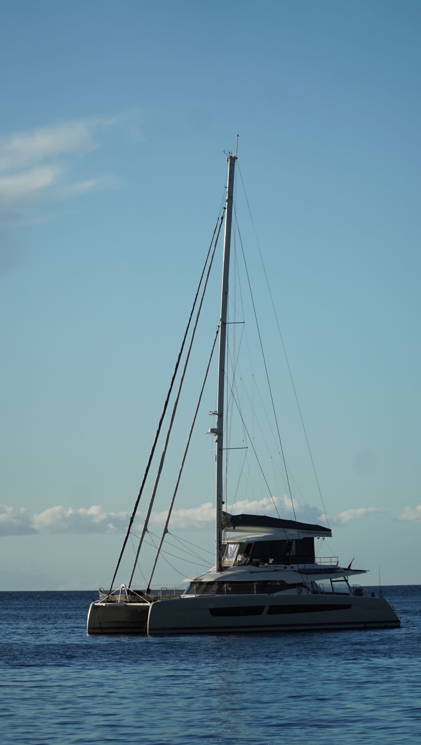 Sailing catamaran with its sails furled, anchored on a calm blue sea under a clear sky