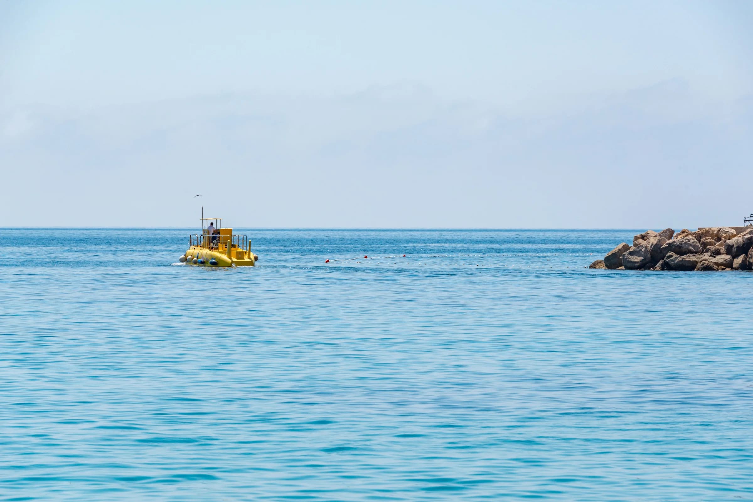 Yellow tourist submarine on the surface of a calm blue sea, next to a rocky breakwater outside Puerto de Mogán